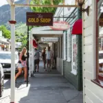 Historic shop signs and pedestrians along the main street footpath in Arrowtown.