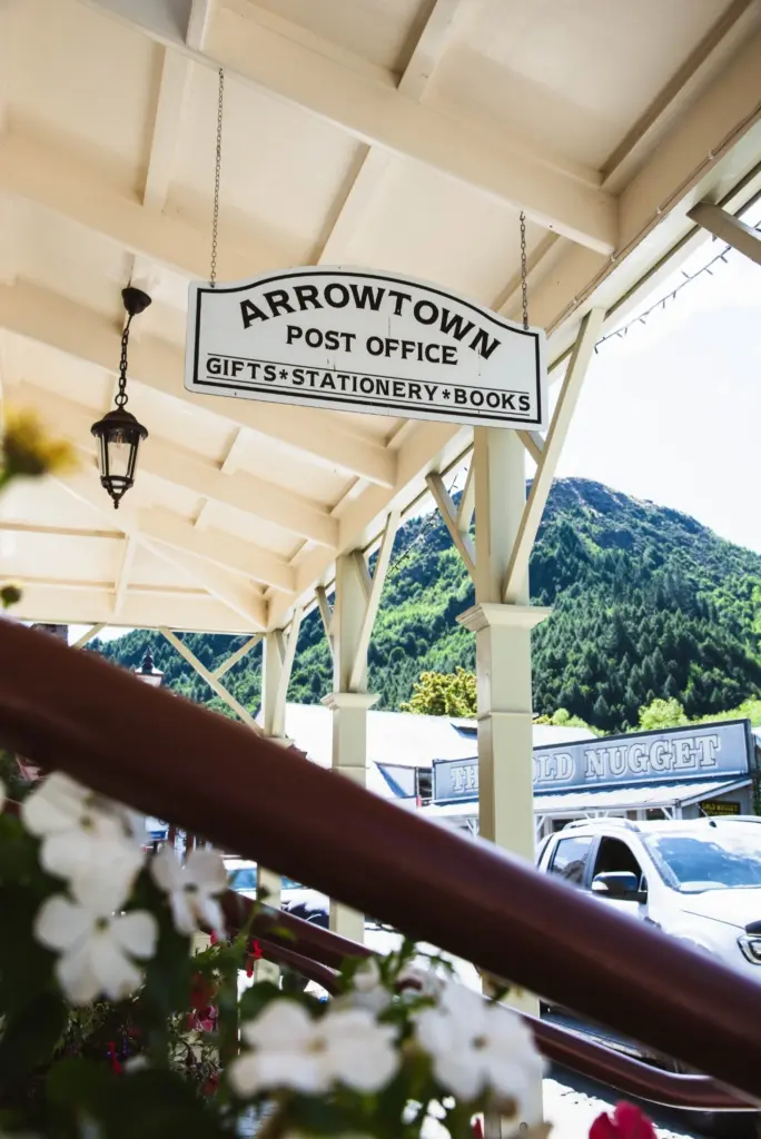Arrowtown Post Office hanging sign under a covered walkway with mountains behind.