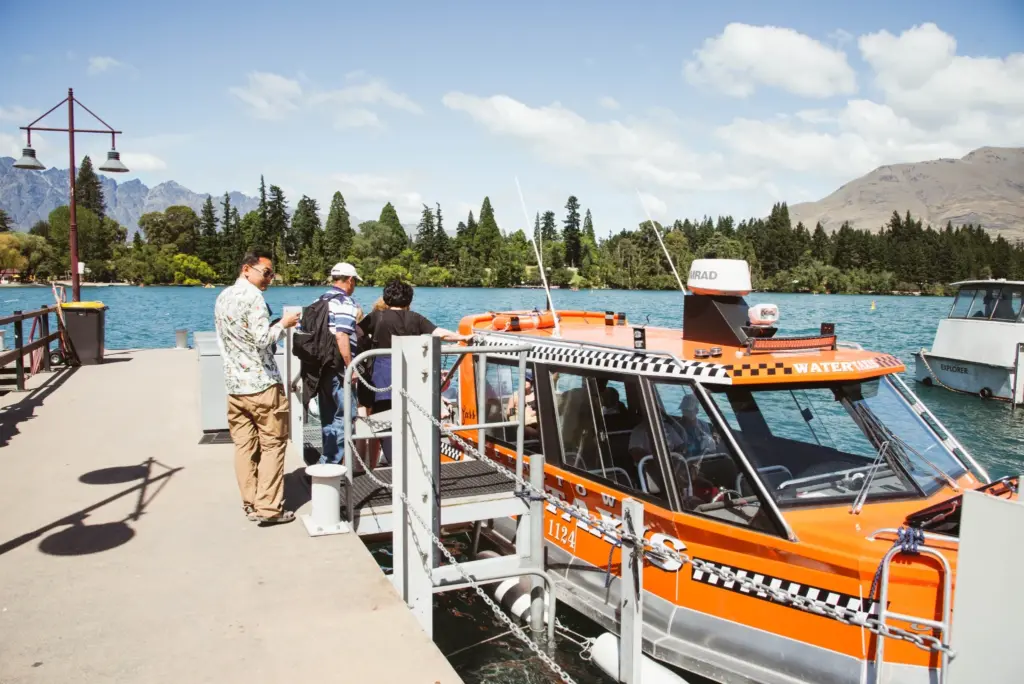Visitors boarding an orange water taxi beside the lake in Queenstown.