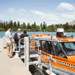 Visitors boarding an orange water taxi beside the lake in Queenstown.