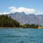 View across blue lake water toward mountains and forest near Queenstown.