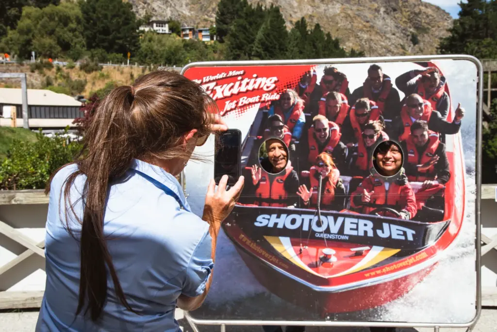 Tour guide taking a photo beside a Shotover Jet display board in Queenstown.