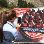 Tour guide taking a photo beside a Shotover Jet display board in Queenstown.