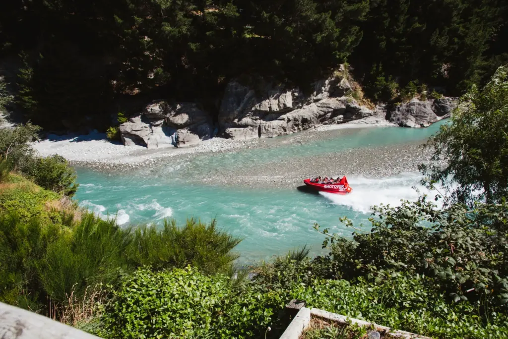 Red Shotover Jet boat speeding through a turquoise river canyon near Queenstown.