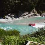 Red Shotover Jet boat speeding through a turquoise river canyon near Queenstown.