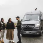 Local guide speaking with guests beside the Milford Sound Business Class tour van